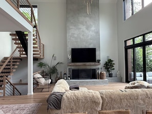 Ein geräumiges Wohnzimmer mit Kamin, einem großen Fernseher und einer Treppe.
