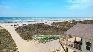 A beach view with a building featuring a deck and outdoor seating. - True Beachfront New Build with Huge Oceanview Deck - Sans Souci Sleeps 12 (Port Aransas)