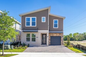 A two-story house with a front garage, a small front yard, and a paved driveway. - Luxury Reunion Resort 6BR Villa Private Pool, Spa & Disney Nearby (Kissimmee)