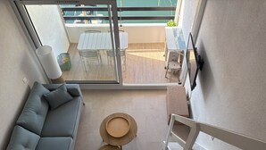 Moderni sisustus, jossa on harmaa sohva, kaksi pyöreää puupöytää ja näkymä ulkoilmabalconille, jossa on pöytä ja tuolit.