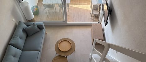 A modern interior with a grey sofa, two round wooden tables, and a view of an outdoor balcony with a table and chairs.