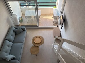 A modern interior with a grey sofa, two round wooden tables, and a view of an outdoor balcony with a table and chairs. - Les Marines du Soleil in Carnon-Plage. (Mauguio)