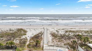 Ein Strand mit Promenade, die zum Meer führt, Sanddünen und blauem Himmel.