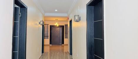 A hallway with a door at the end, a light fixture above, and a wall-mounted light on the left.
