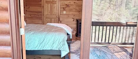 A wooden cabin bedroom with a bed, a door, and a view of a forest through a glass door.