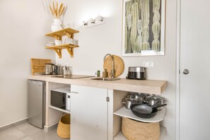 A compact kitchen with a built-in refrigerator, a microwave, and a sink. There are wooden shelves above the counter and a woven basket below. - Studio Ariba  2person studio in Jan Thiel with swimming pool (Jan Thiel)
