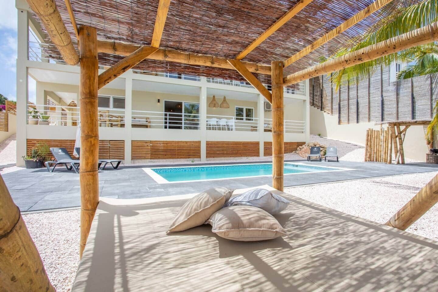 A poolside area with a pergola, lounge chairs, and a view of a modern building with a pool.