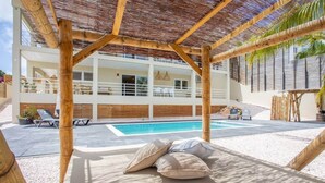 Un espace aménagé au bord de la piscine, avec une pergola, des chaises longues et une vue sur un bâtiment moderne doté d’une piscine.