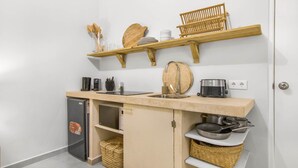 Une cuisine compacte dotée d’un réfrigérateur intégré, d’un évier et d’étagères en bois au-dessus, où sont rangés la vaisselle et les ustensiles.