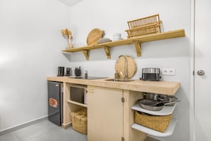 A compact kitchen with a built-in refrigerator, a sink, and wooden shelves above holding dishes and utensils. - Studio Mei Mei – studio within walking distance of Jan Thiel (Jan Thiel)