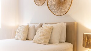 Una cama con cabecera color beige, ropa de cama blanca y almohadas decorativas.