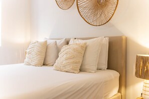 Ein Bett mit hellem, beigefarbenen Kopfteil, weißer Bettwäsche und Zierkissen.