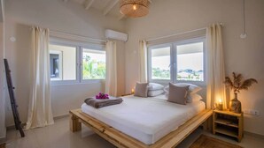 A bedroom with a wooden bed, two bedside tables, a hanging light fixture, and a window with curtains. - Casa Ariba 6 person penthouse with swimming pool in JT (Jan Thiel)