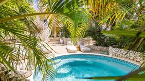 A swimming pool with a stone border, surrounded by palm trees and a stone wall. - Cas Agave 2bedroom apartment with swimming pool in Jan Thiel (Jan Thiel)