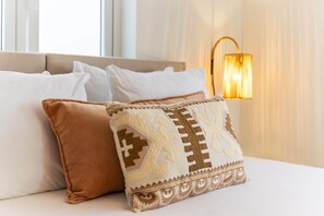Ein Bett mit weißen und braunen Kissen, einem beige gefärbten Kopfteil und einer Wandlampe.