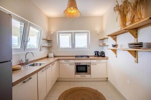 A modern kitchen with a stove, oven, sink, and wooden shelves. - Casa Mei Mei – 8-person apartment in Jan Thiel with balcony (Jan Thiel)