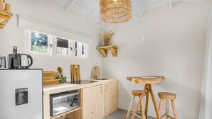 Une cuisine compacte équipée d’un lave-vaisselle encastré, d’une machine à café, de tabourets en bois et d’un luminaire suspendu.