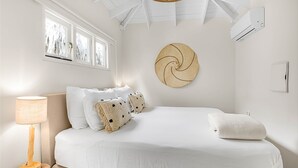 Une chambre à coucher comprenant un lit, un climatiseur fixé au mur, une fenêtre avec des stores et un élément décoratif mural.