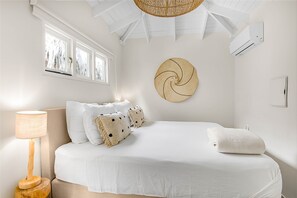 Ein Schlafzimmer mit einem Bett, einer Wand-Klimaanlage, einem Fenster mit Jalousien und einem Wanddekor.