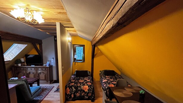 Una habitación compacta con suelo de madera, una cama con ropa de cama floral, una pequeña mesa con sillas y una ventana con vistas al exterior.
