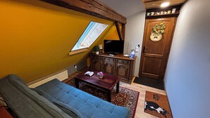Habitación con sofá, una mesita, televisión, armario de madera, puerta con un símbolo de mascota y ventana con vistas.
