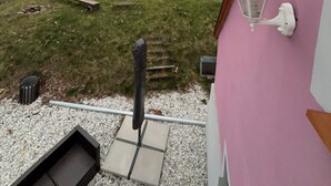 Vista desde un edificio rosa con pared exterior blanca, una terraza de madera, una escalera de metal y un sendero de grava que conduce a un campo verde.