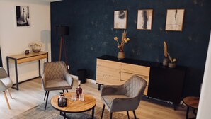 A modern living room with a dark blue accent wall, a wooden coffee table, two grey upholstered chairs, a wooden side table, and a black floor lamp. - Penion 44444 (Schkopau)