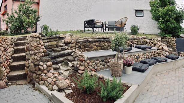 A stone retaining wall with steps, outdoor seating, and planters. - Penion 44444 (Schkopau)