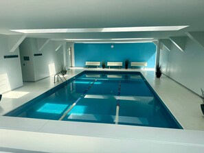 A modern indoor swimming pool with clear lane dividers, benches along the walls, and potted plants. - Dream Condo in the Heart of Mexico City (Ciudad de México)