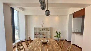 Ein Essbereich mit Holztisch, Stühlen, einer Schüssel in der Mitte, einer Topfpflanze und einer weißen Regaleinheit mit Dekoration.