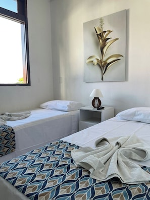 Een hotelkamer met twee bedden, een raam, een nachtkastje met lamp en een aan de muur bevestigd kunstwerk.