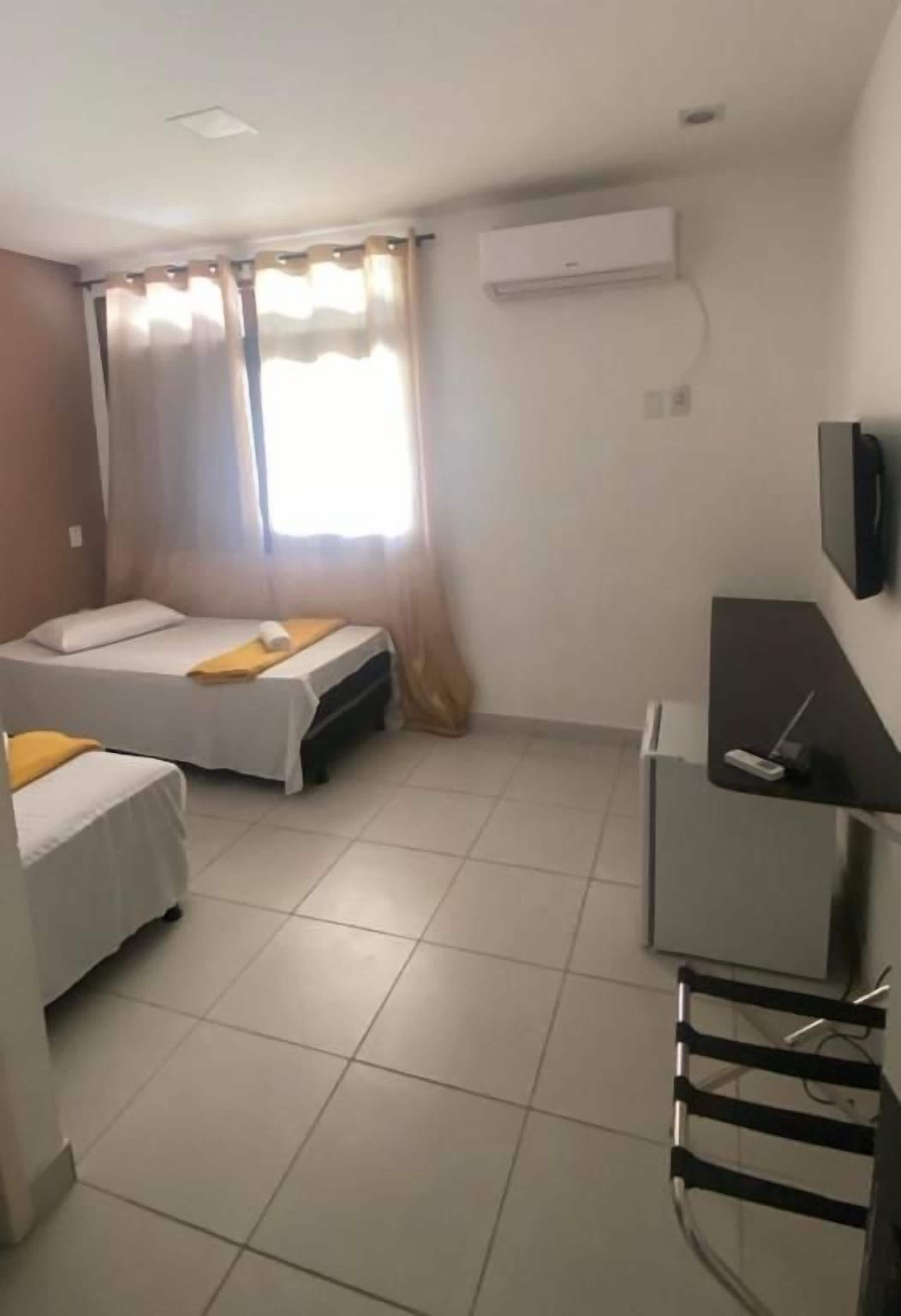 Una habitación con dos camas, un escritorio, un televisor y una ventana con cortinas.