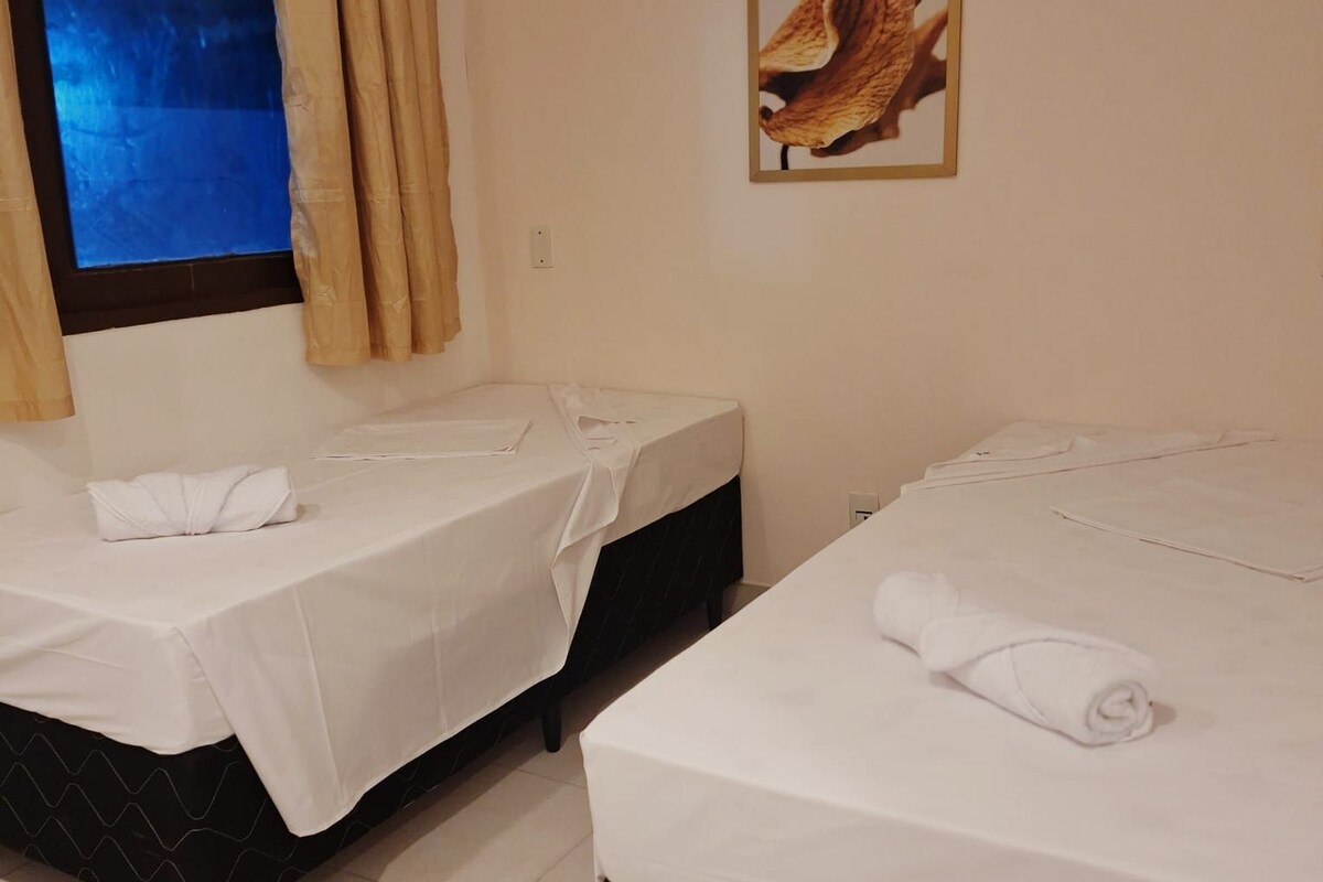 Two single beds with white linens, a window with curtains, and a framed picture on the wall.