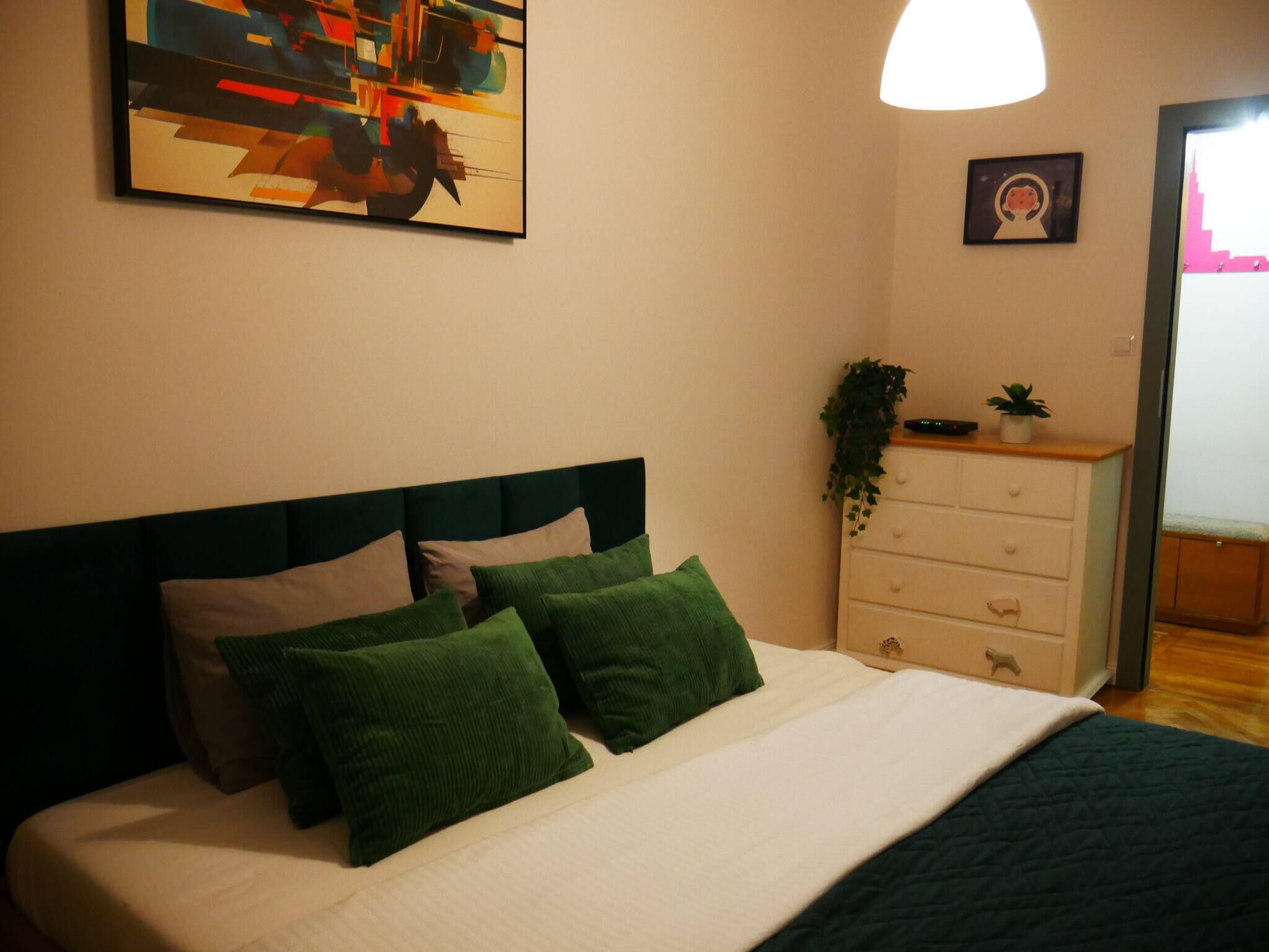 Un dormitorio con una cama, un aparador, un cuadro y una planta.