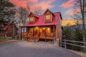 A log cabin with a red roof, a porch, and a staircase leading to the entrance. - AmazingMtnViews-Pool-3Suites-HotTub-GameRoom-CentralLocation (Sevierville)