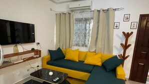 Ein Wohnzimmer mit Ecksofa, Flachbildfernseher, Deckenventilator und einem Fenster mit Vorhängen.