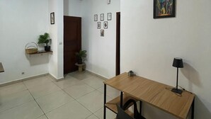 Ein Zimmer mit Holztisch, schwarzem Stuhl, Lampe, Topfpflanze und einem gerahmten Bild an der Wand.
