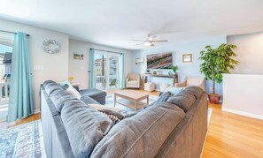 Ein Wohnzimmer mit grauem Ecksofa, einem Couchtisch, einem Deckenventilator und einer Topfpflanze.