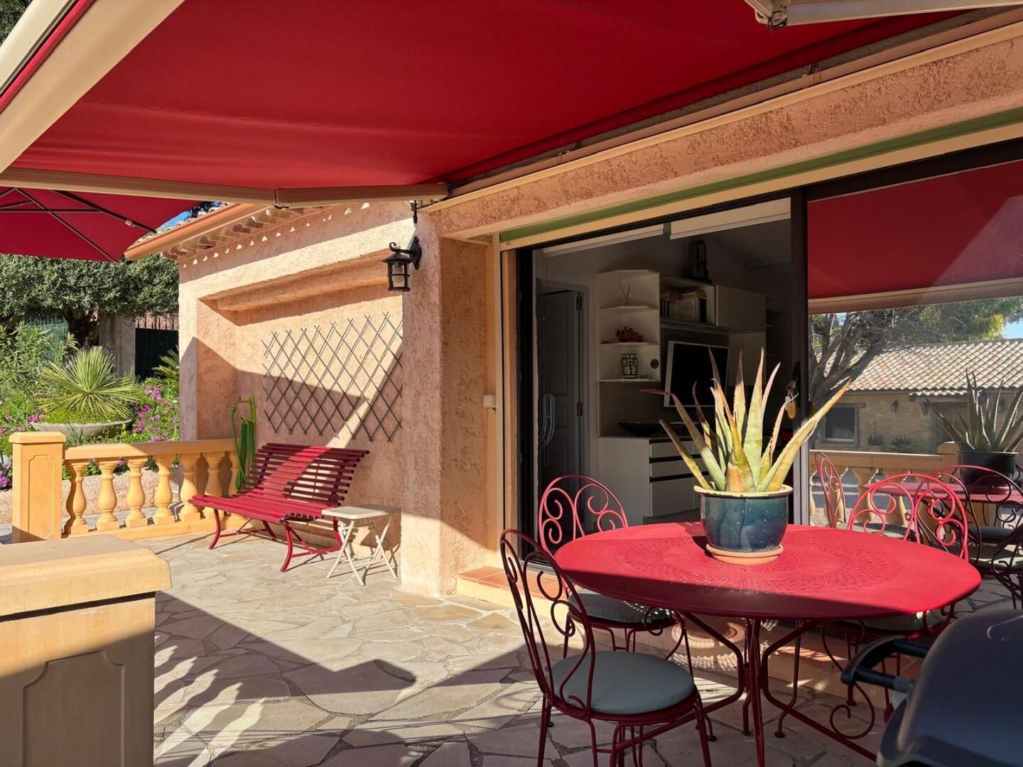 Eine Terrasse im Freien mit einem roten Tisch und Stühlen, einem Blumentopf und einem roten Markisenvorzelt.