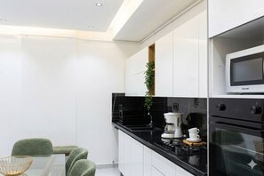Una cocina moderna con armarios blancos, encimera negra, cafetera y horno.