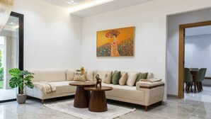 Een moderne woonkamer met een beige bank, twee houten bijzettafels, een groot schilderij en een potplant.