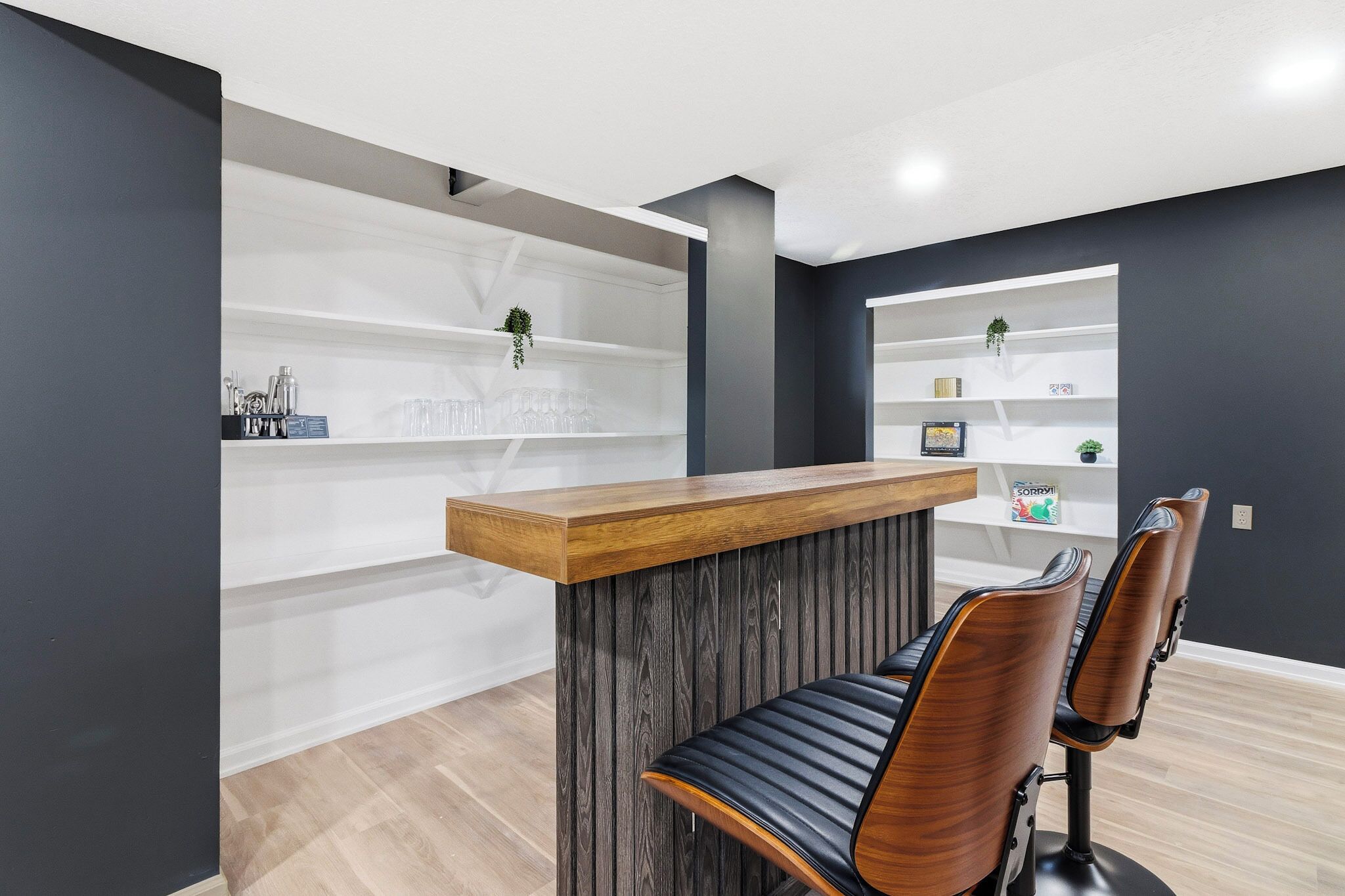 A reception desk with a wooden top and a dark wood panel, two leather chairs, and white shelving units with decorative items.