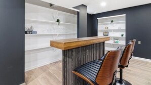 A reception desk with a wooden top and a dark wood panel, two leather chairs, and white shelving units with decorative items. - Luxury Fishers,IN Home - 4BR • Fully Renovated • Finished Basement • WiFi (Fishers)