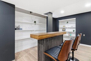 Un mostrador de recepción con encimera de madera y panel de madera oscura, dos sillones de cuero y estanterías blancas con objetos decorativos.