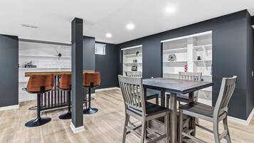 A modern dining area with a wooden table and chairs, a bar area with stools, and built-in shelves with decorative items.