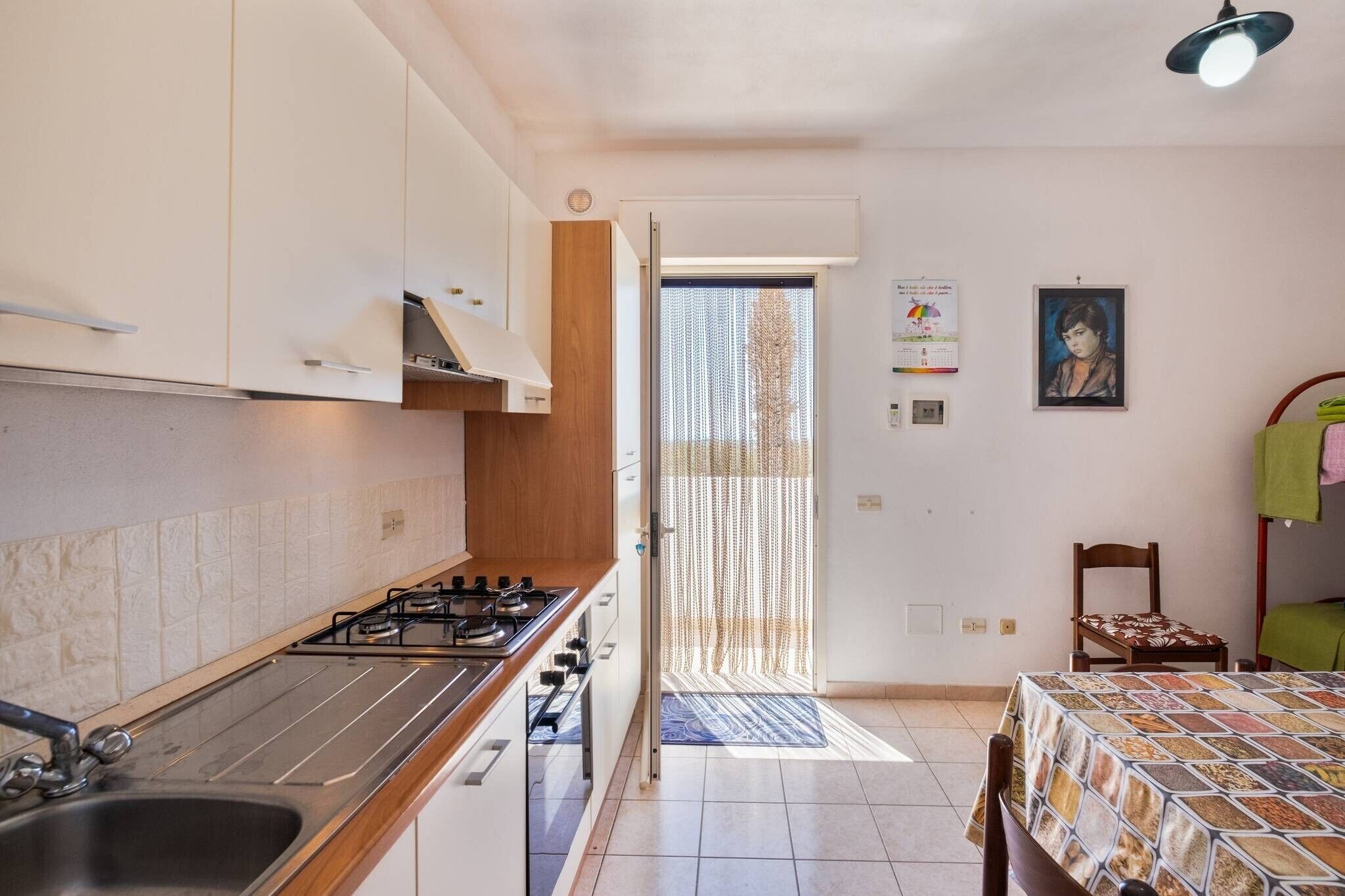 Cuina amb fogó de gas, un rentaplat i armaris. Hi ha una zona de menjador amb taula i cadires.