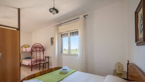 A bedroom with a bunk bed, a single bed, a bedside table with a lamp, a window with curtains, and a wardrobe. - Marubium - Scorcialupi (Maruggio)