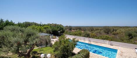 A swimming pool with a clear view of the surrounding landscape, a pathway, and some outdoor seating.