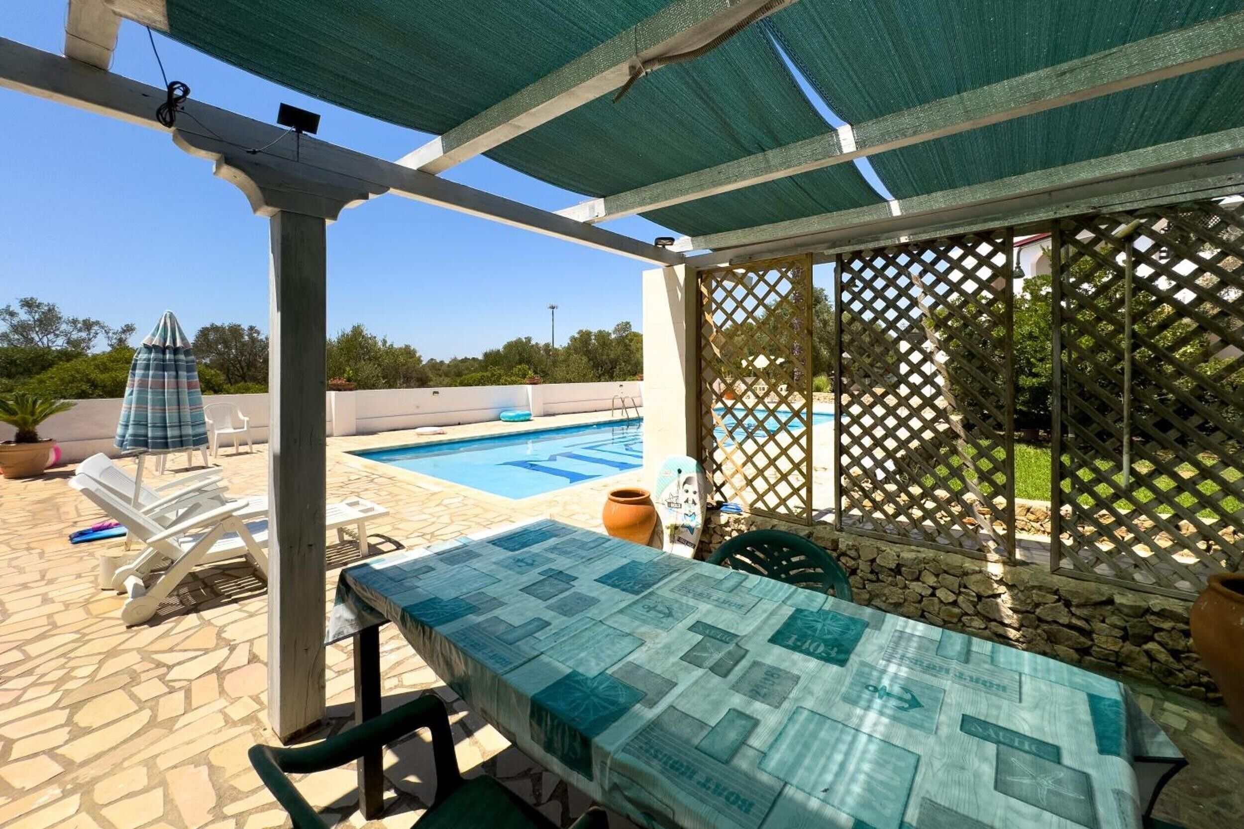 Un espace extérieur abrité comprenant une piscine, des chaises longues et une table recouverte d’une nappe à motifs.