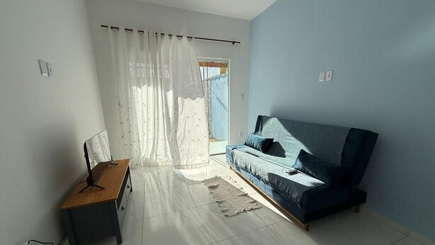 Una habitación con un sofá azul, un escritorio de madera y un ventanal con cortinas.